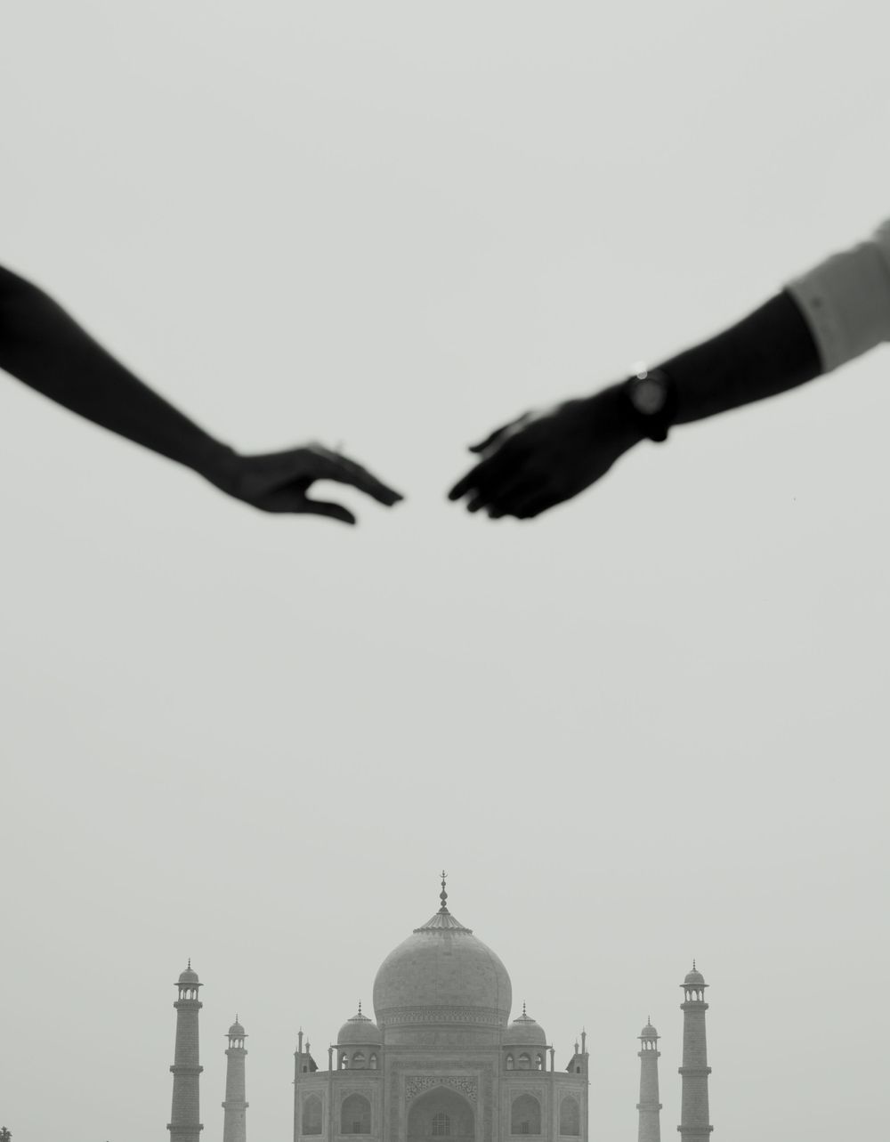 Reaching hands silhouetted against the iconic Taj Mahal in black and white.