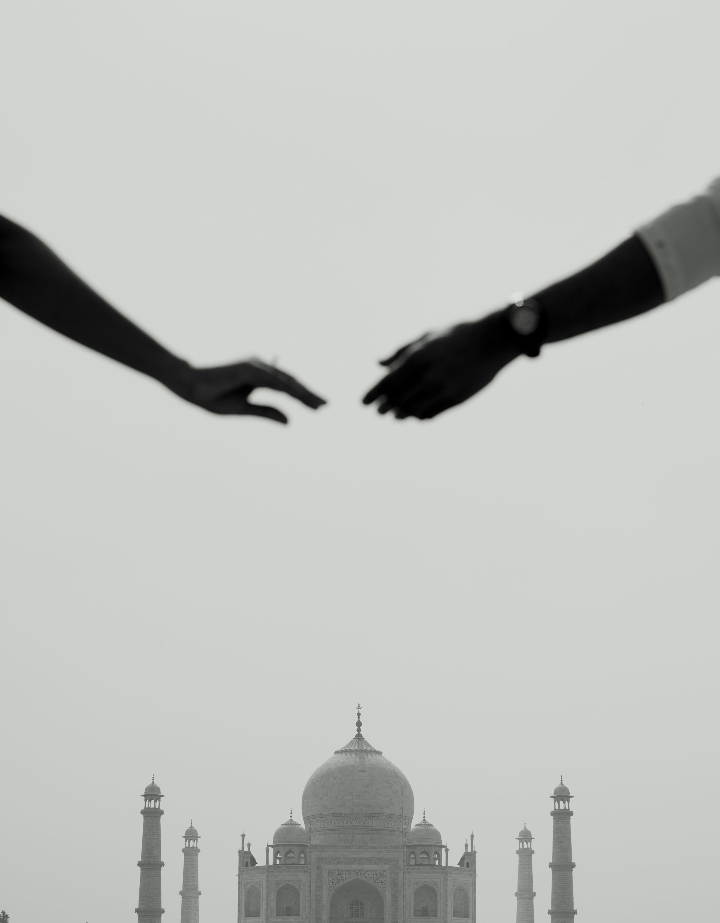 Reaching hands silhouetted against the iconic Taj Mahal in black and white.