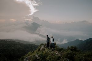 Couple sharing a special moment atop a misty mountain peak during sunset.