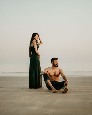 Artistic beach portrait with couple in contrasting poses against minimal backdrop.