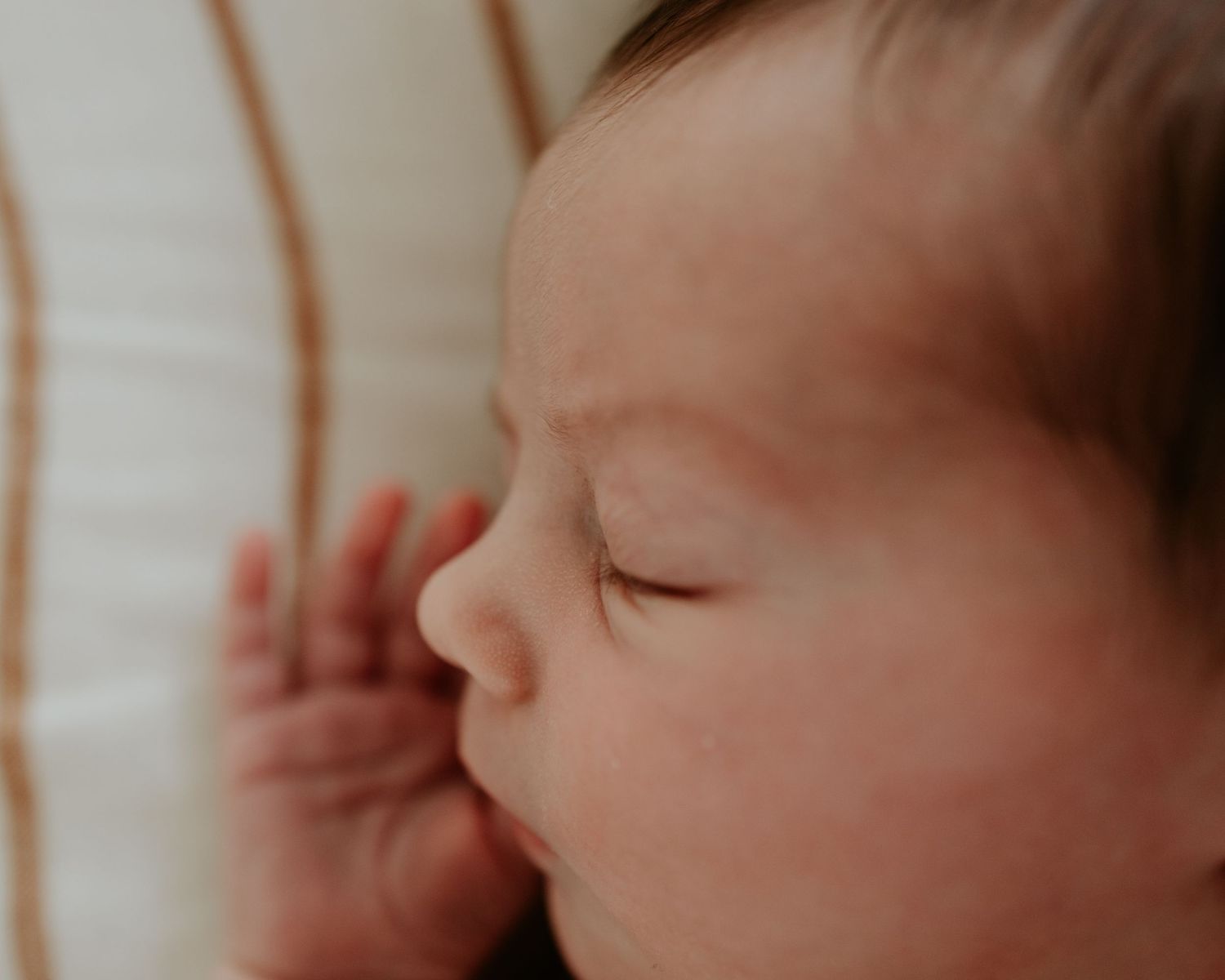 Peaceful sleeping newborn baby wearing knitted beige overalls rests on soft gray blanket.