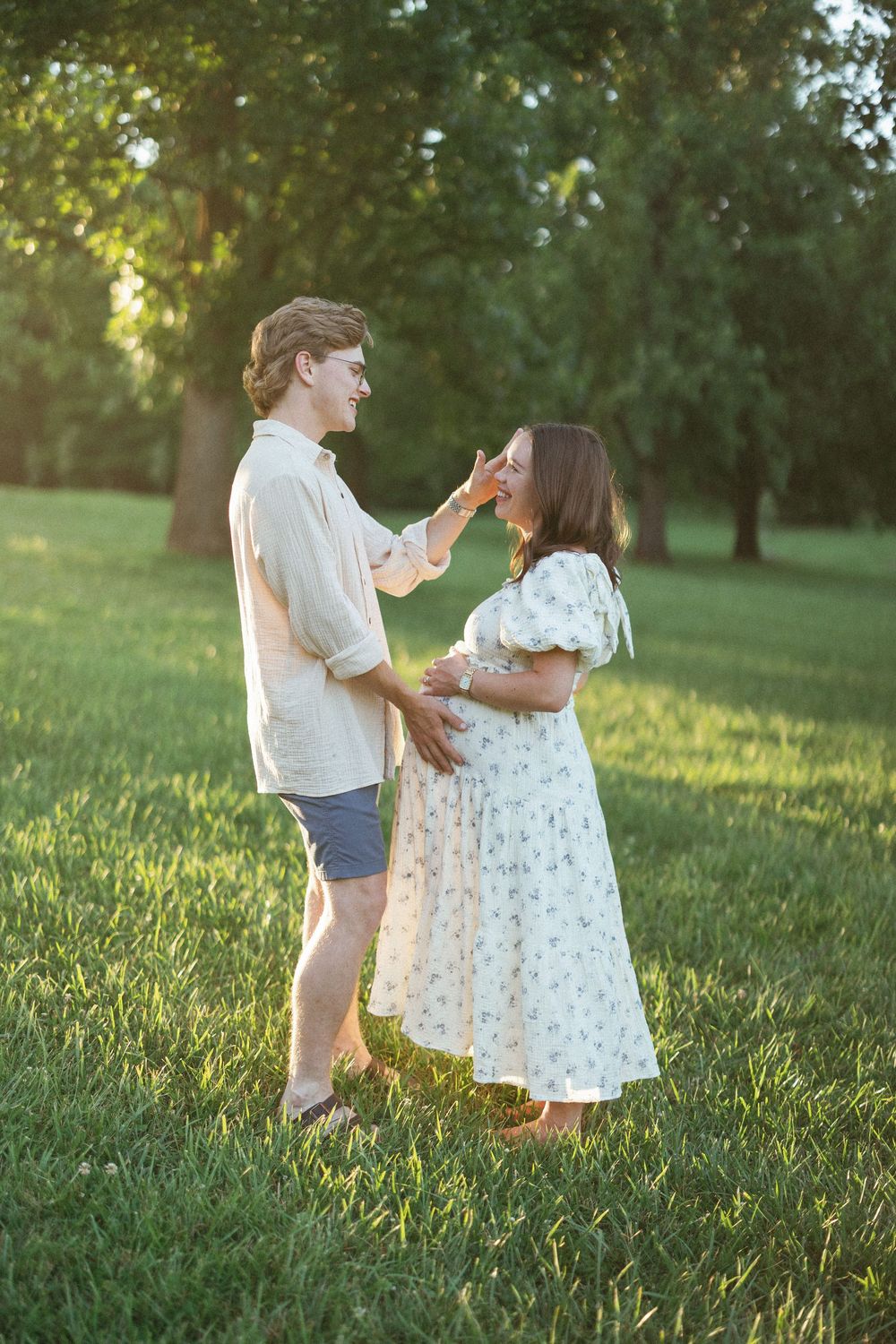 A couple shares a tender moment in a sunlit park, with the man gently touching the pregnant woman's face.