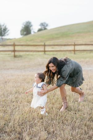 A playful moment in a grassy field with a fence and rolling hills in the background.