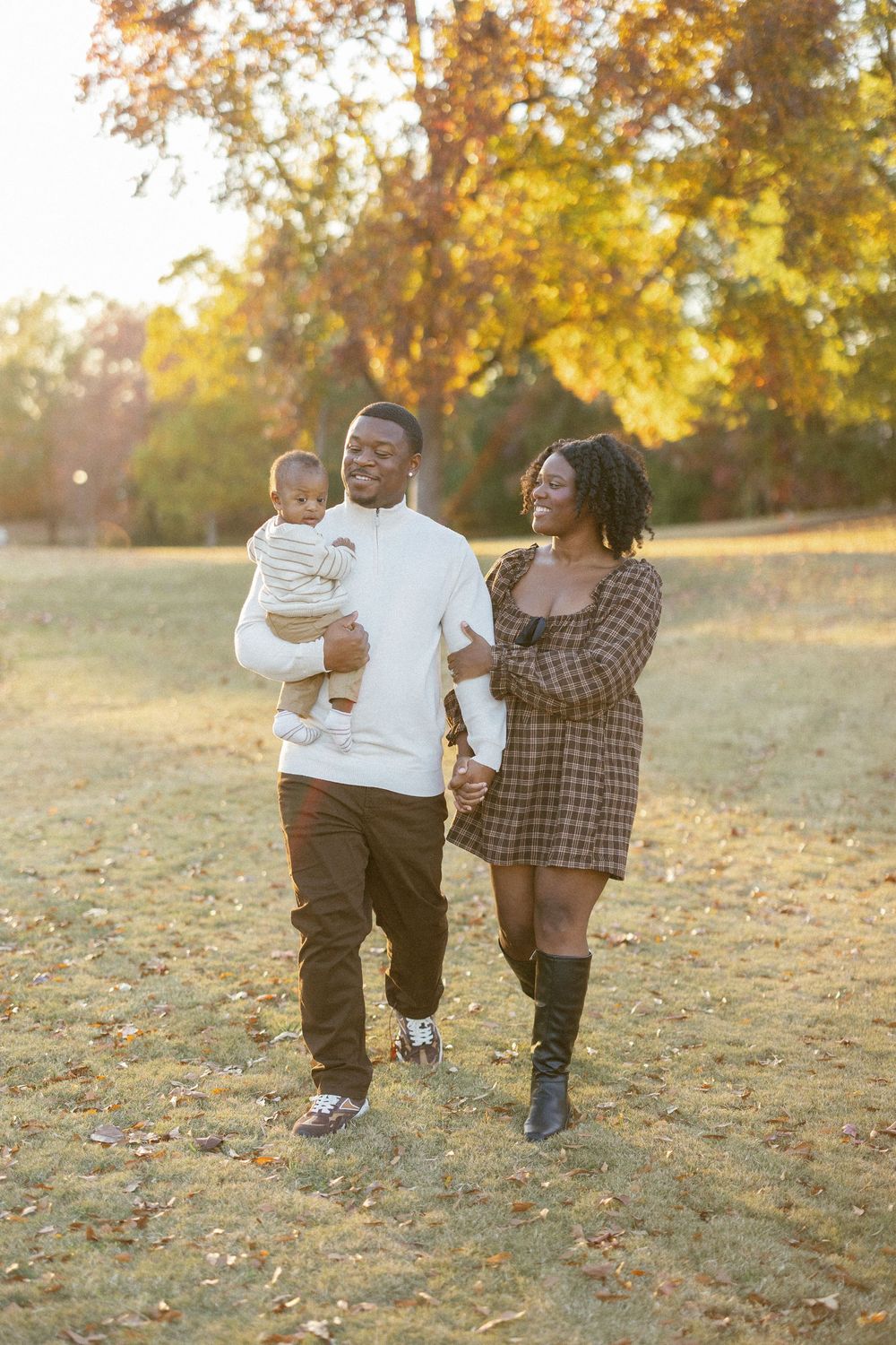 A family walks together through a sun-drenched autumn field with golden leaves scattered on the ground.