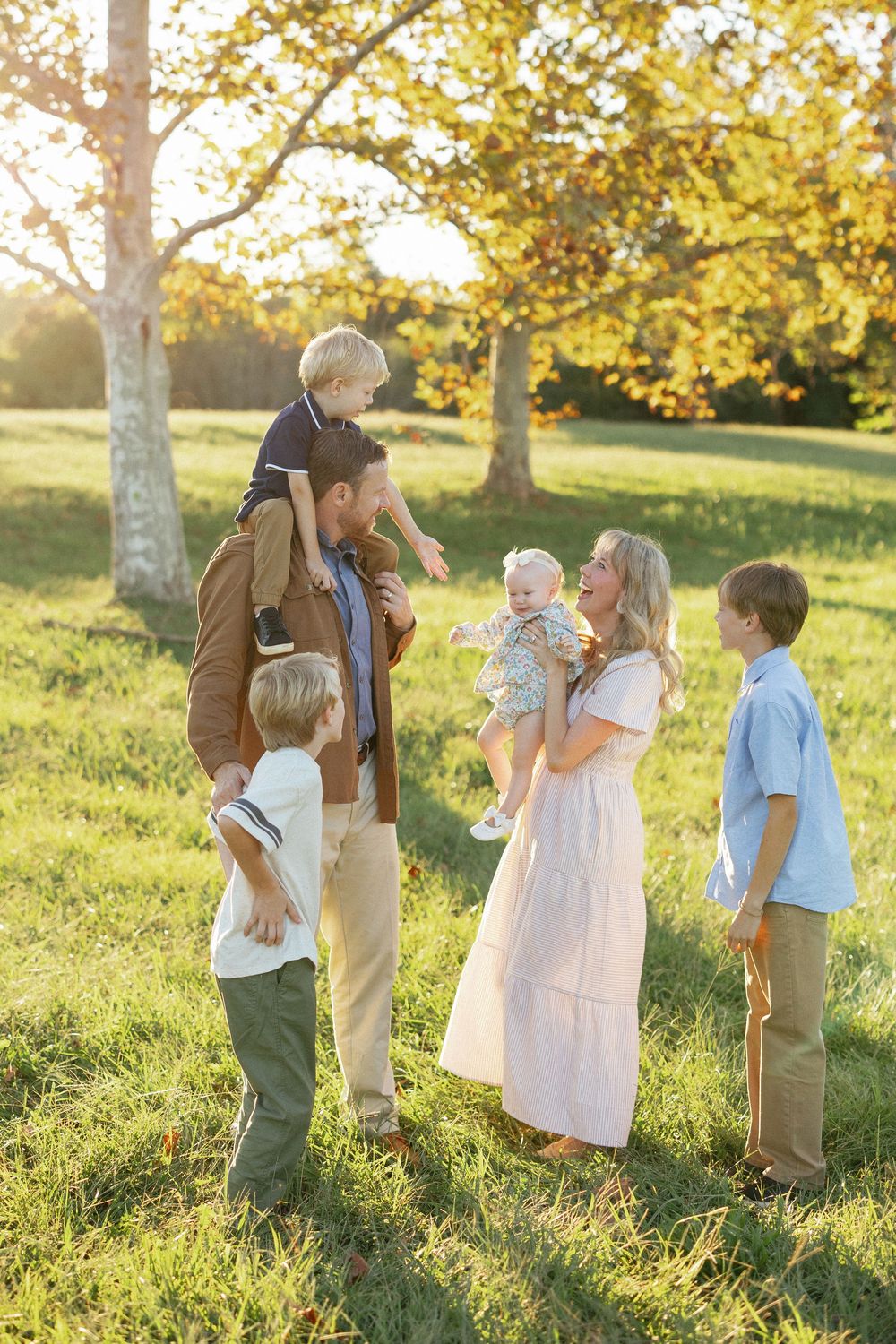 A happy family with four young children enjoys a sunny autumn day outdoors in a lush green park.