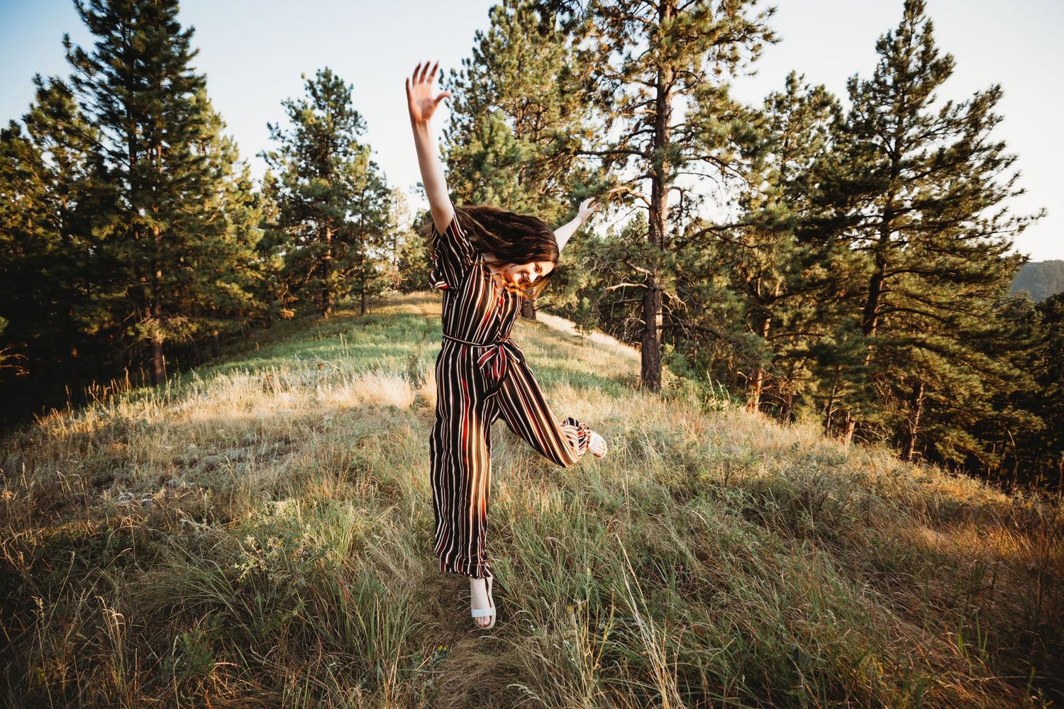 Senior girl in black jumpsuit jumps in air surrounded by trees in Dickson, TN