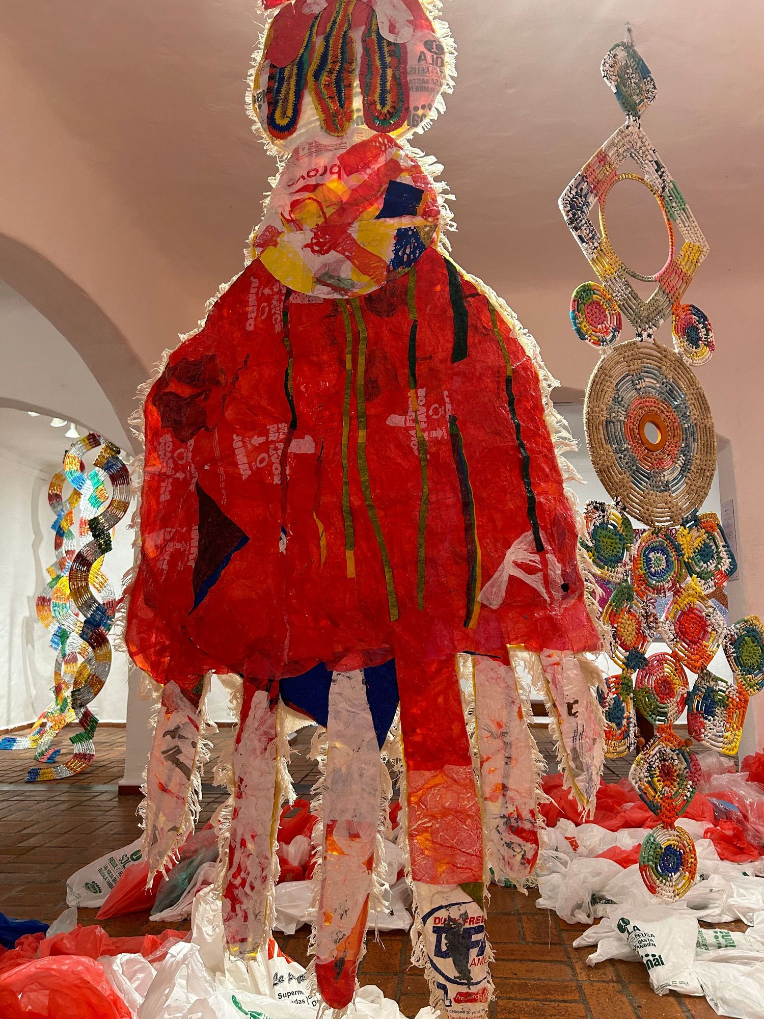 Hanging art installation with red textile figure and decorative circular elements.