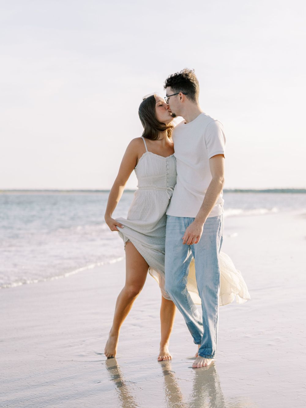 A couple embraces lovingly on a beach with waves in the background.
