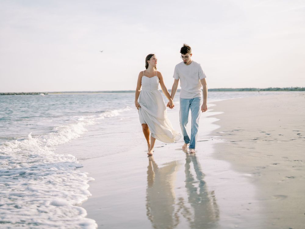 A couple walking hand in hand along the water's edge on a pristine beach.