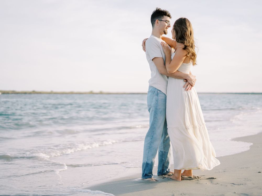 Intimate beach photoshoot showing couple in white and denim against ocean backdrop.
