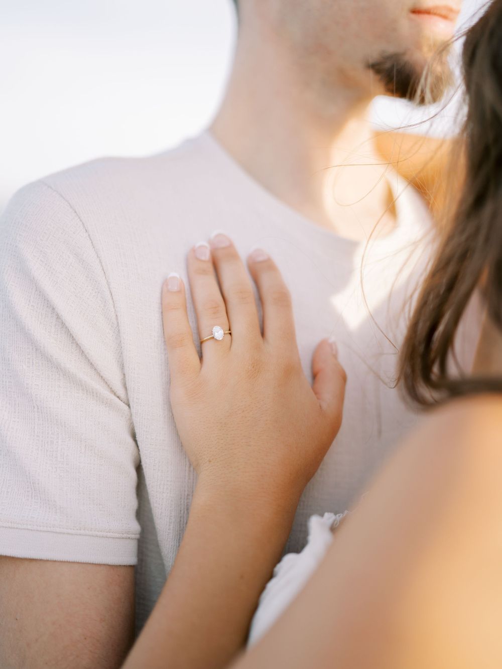 Close up of engagement ring on hand resting against white shirt.