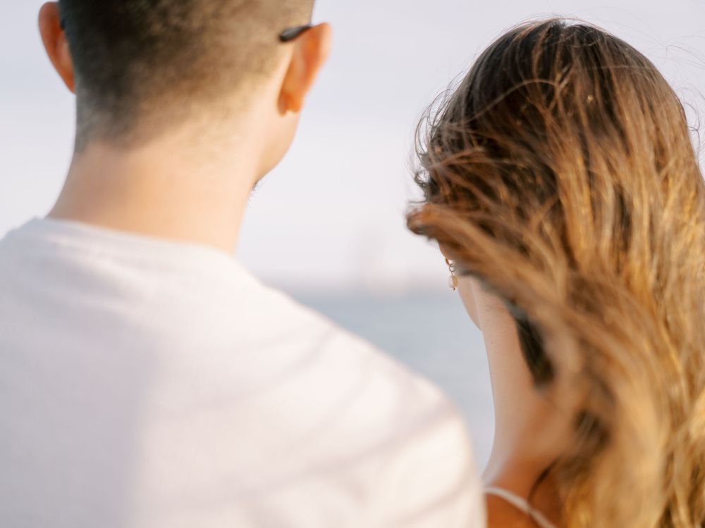 Back view portrait of couple by the ocean with hair blowing in wind.