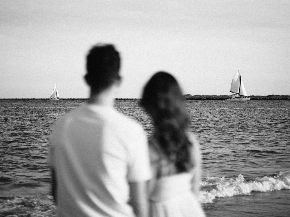 Silhouetted couple watching sailboats on horizon in black and white.
