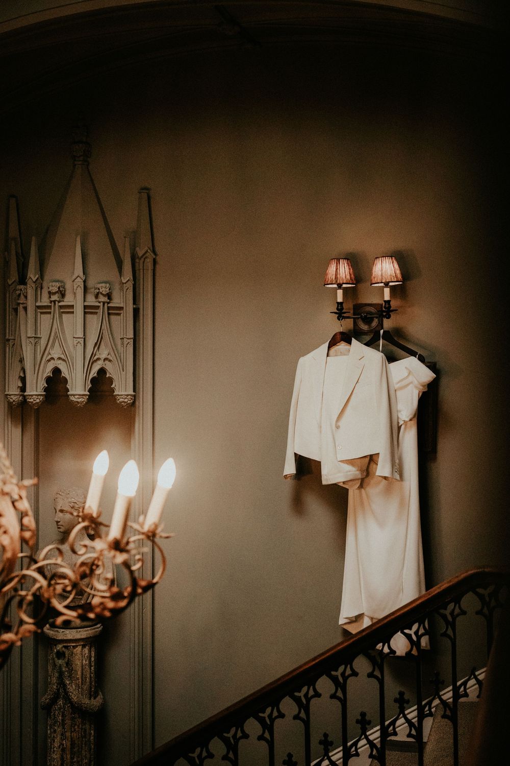 Elegant bridal outfits hang on a wall sconce in a Gothic-style staircase interior.