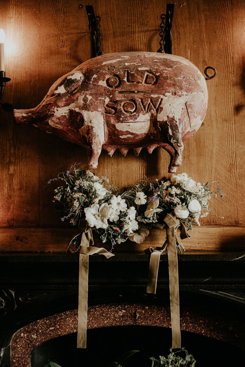 Rustic wedding decor featuring white floral bouquets on a wooden stool beneath an antique carved pig sign reading Old Sow.
