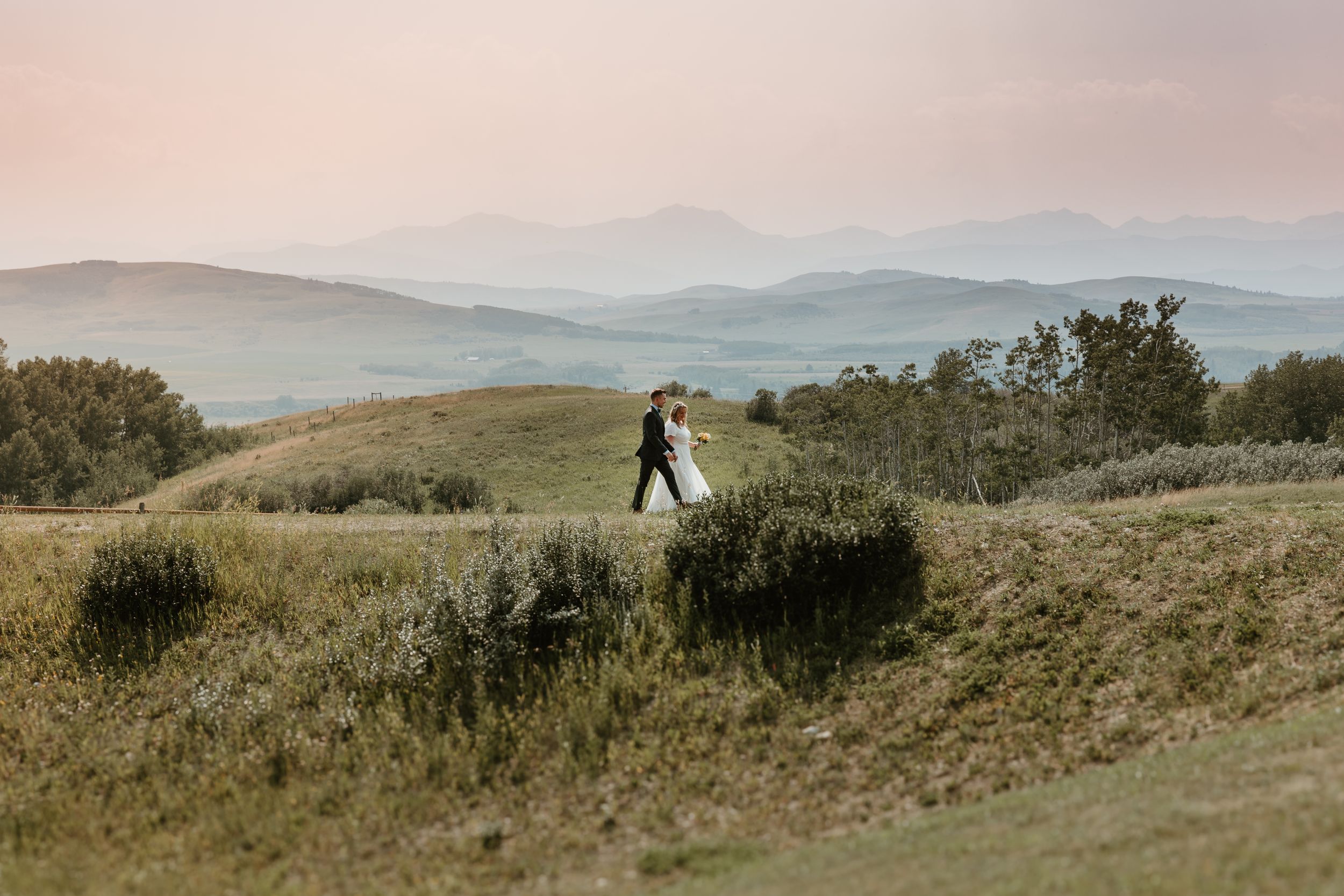 Bride and groom walking in front of the Rocky mountains, capturing the gorgeous country landscape at Willow Hill Lodge