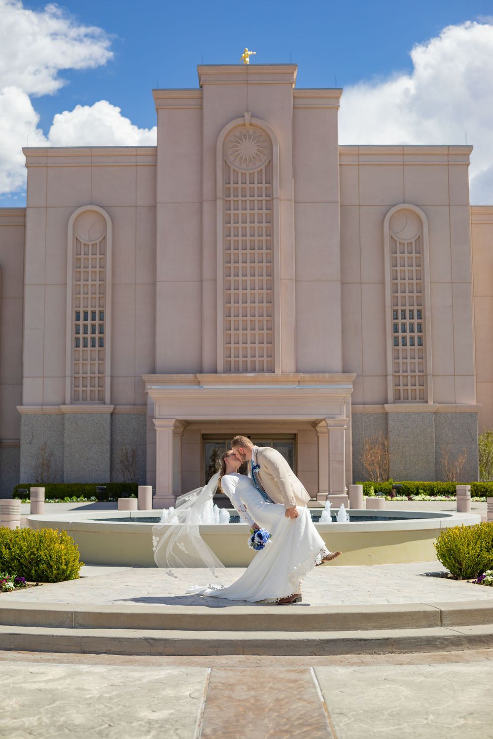 Newlyweds share romantic dance pose outside ornate white temple building.