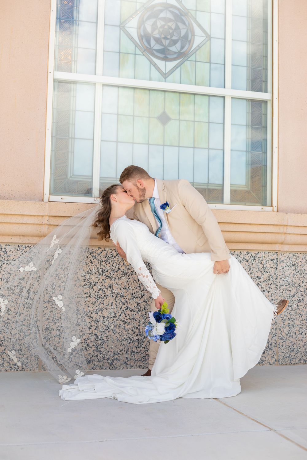 Romantic dip kiss between newlyweds under decorative window with flowing veil.