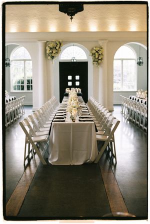 Elegant wedding reception setup with long white-clothed tables and chairs arranged in rows under soft lighting.