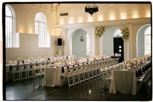 Elegant white banquet hall with arched windows and rows of tables set for a formal event in classic style.