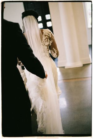 Wedding dress detail showing delicate white lace and tulle fabric against a dark floor.