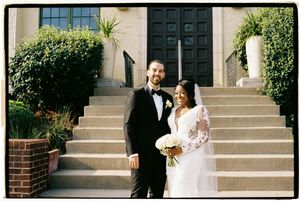 A wedding couple shares joyful moments on stone steps outside a building with black doors and greenery.
