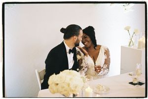 A joyful couple shares an intimate moment at their wedding reception table decorated with white floral centerpieces.