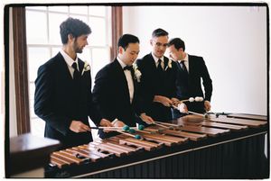 Four musicians in formal black suits perform on a wooden marimba during an elegant indoor event.