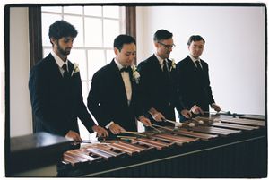 Musicians in formal attire perform on marimbas in a bright indoor space.