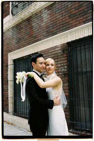 Wedding couple embracing against a brick wall with black window bars creating geometric patterns.