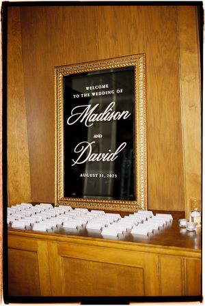Wedding place cards and welcome signs displayed on wooden shelves with elegant black and white typography.