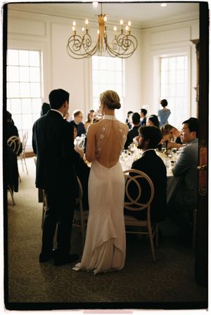 Wedding reception guests mingle in an elegant white room with chandeliers and soft lighting creating an intimate atmosphere.