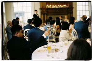 People gathered at tables in a restaurant for a formal dining event with wine glasses and natural lighting.