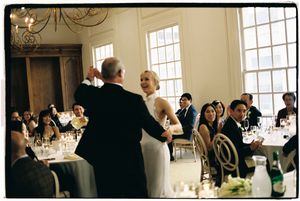 Wedding reception guests seated at elegant tables in a bright sunlit venue with white decor.