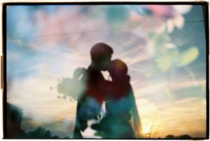 A silhouetted couple embraces against a dreamy sunset sky with soft bokeh lights in the background.