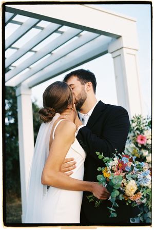 A romantic moment under a white pergola with colorful floral bouquet.