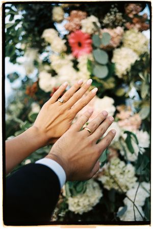 Close-up of hands with wedding rings against floral backdrop showing romantic moment.
