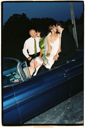 People climbing into a vintage blue convertible car at dusk or nighttime.