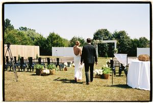 An outdoor wedding ceremony setup with white chairs and floral arrangements on a grassy lawn under trees.