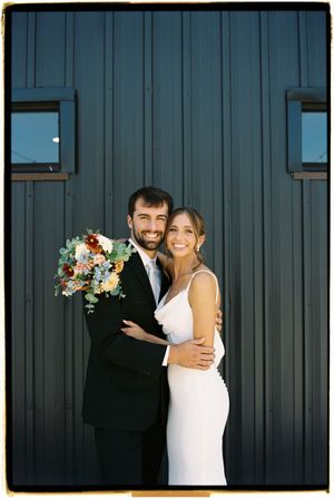 A couple embraces against a dark blue wall during their wedding celebration.