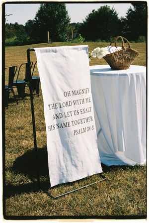 White banners with religious text from Psalm 34:3 hang on a clothesline outdoors against a natural backdrop.