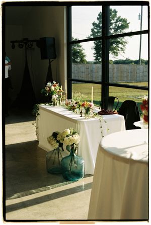 Elegant floral arrangements and white tablecloths in a sunlit room create a romantic wedding reception setting.