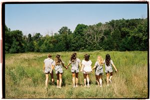A group of people walk in a line through a grassy meadow on a sunny summer day.