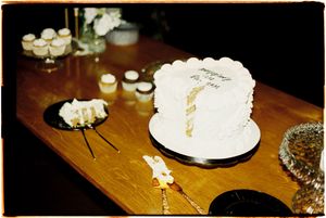 White birthday cake with candles and sparklers glowing on a wooden table in dim lighting.