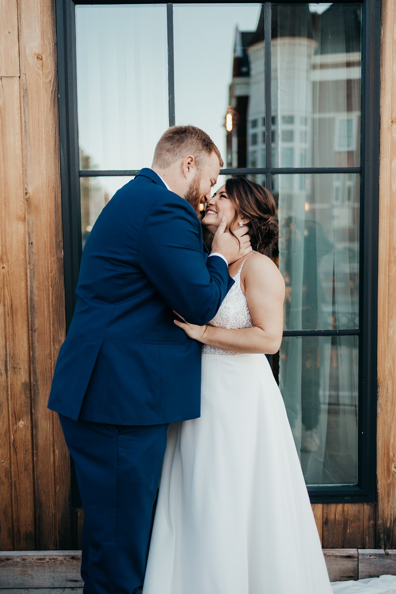 groom kissing brides forhead in front of big windows
