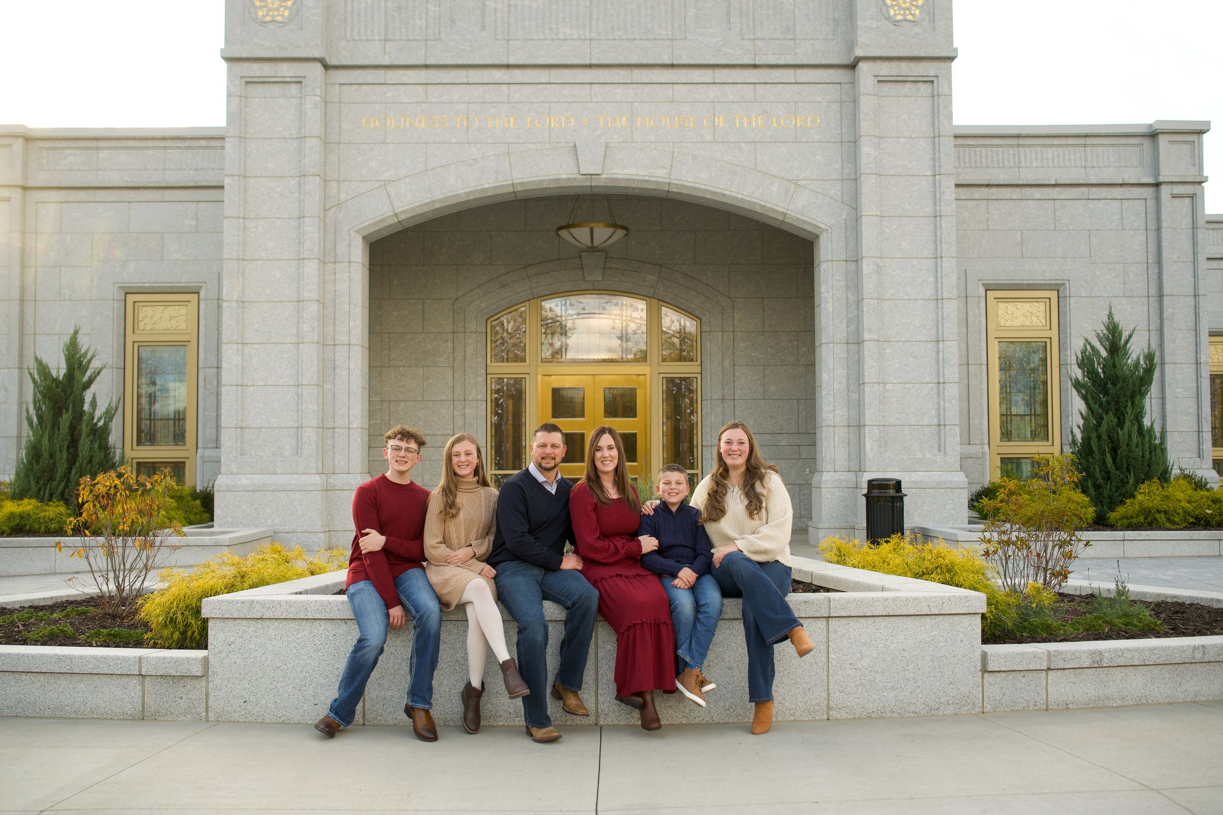 Family of seven posing together outside a grand stone temple entrance with golden doors and manicured grounds.