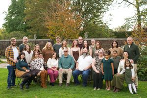 Large family group portrait outdoors in autumn garden, smiling adults and children posed together on green lawn.