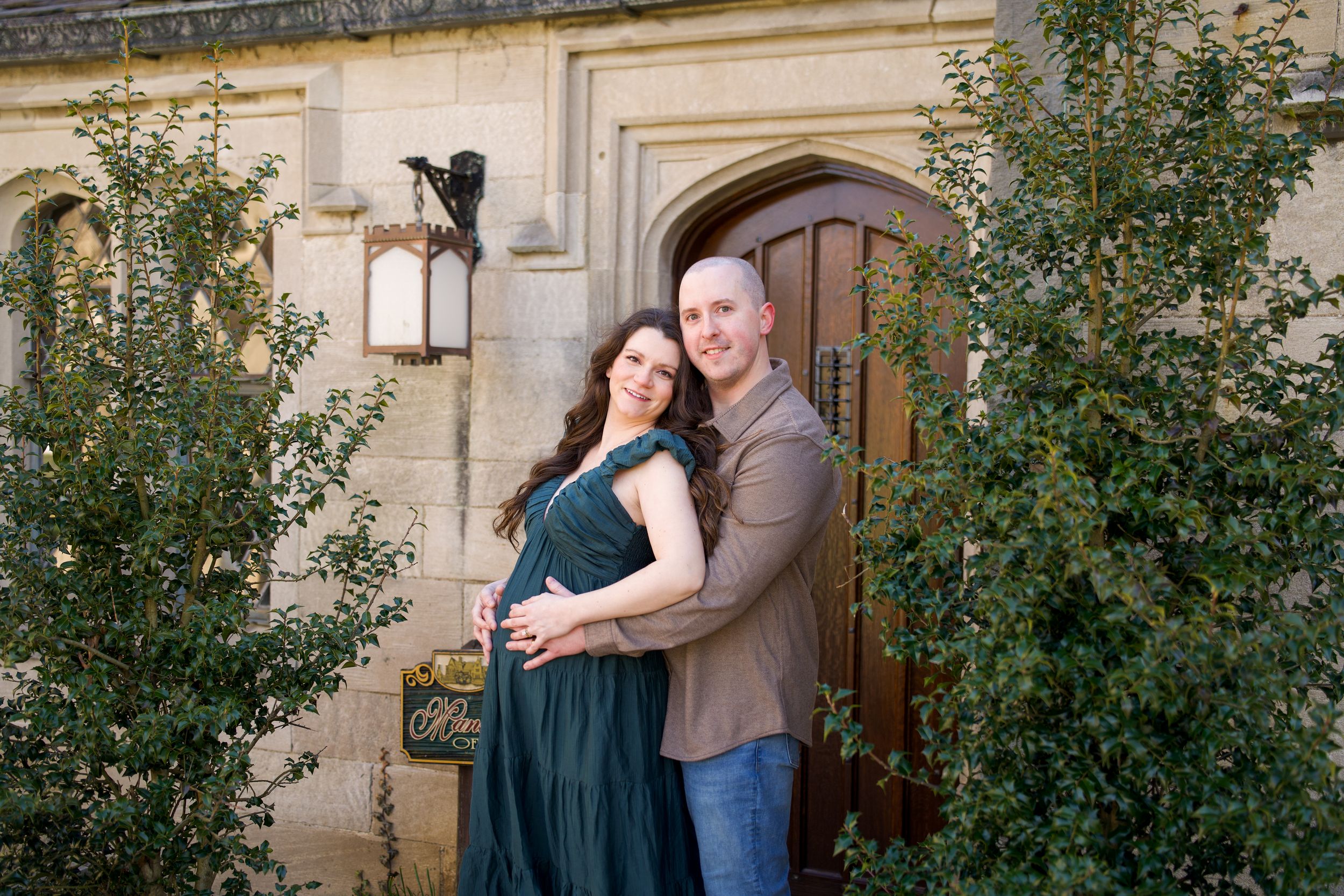 Couple embracing in front of an elegant stone building entrance, woman in green gown, man in brown shirt and jeans.