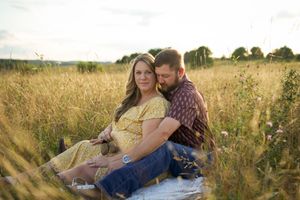 Couple sitting together on blanket in golden sunlit meadow during sunset photography session.