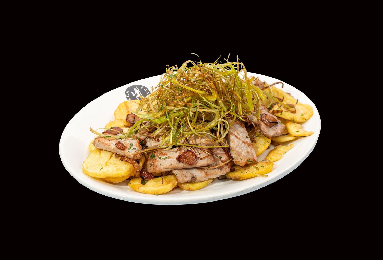 Carne asada en rodajas finas cubierta con crujientes puerros fritos y patatas servida en un plato ovalado blanco. Tierra Astur